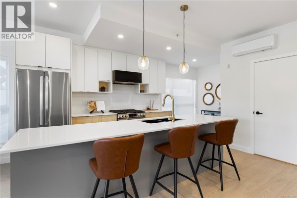 Modern kitchen island with sink, pendant lighting, and open layout to living area. - 104 2629 Millstream Rd, Langford