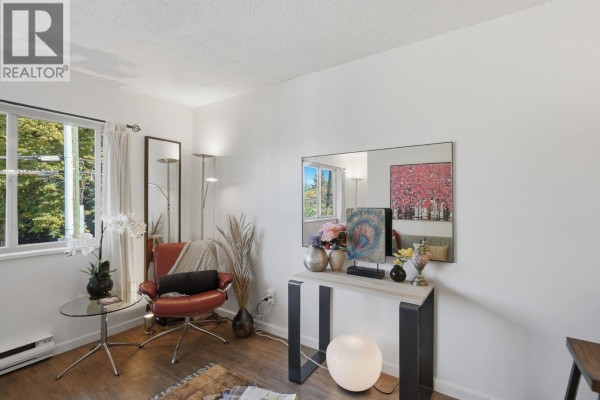 Living area featuring a red accent chair, console table with decorative items, and a large mirror. - 104 3465 Glen Drive, Vancouver