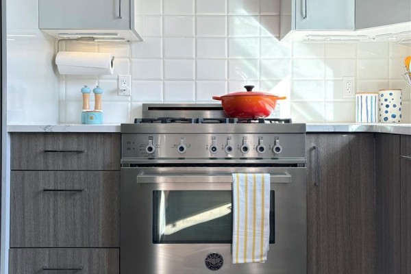 Stainless steel gas range with oven and red pot in a kitchen with white tile backsplash. - 104 3999 Cedar Hill Rd, Saanich