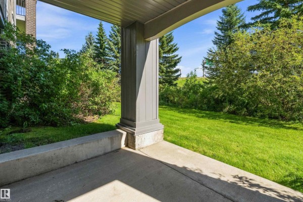 Concrete patio with a view of a grassy lawn and mature trees under a blue sky. - #104 630 Mcallister Lo Sw, Edmonton