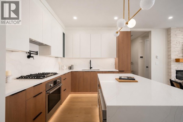 Modern kitchen with white quartz countertops, two-toned wood cabinets, and an island with pendant lighting. - 104 901 Edgar Avenue, Coquitlam