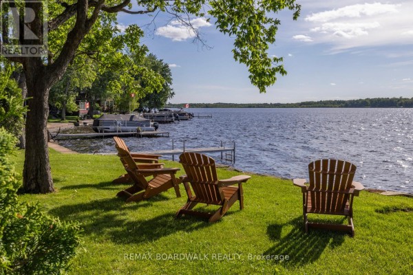 Wooden Adirondack chairs on a lawn facing a lake with docks and boats to the left. - 104 Avenue 4a, Beckwith