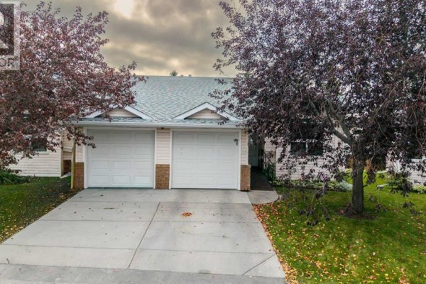 Front exterior of townhouse complex with two garage doors and a paved driveway. - 104 Catalina Circle Ne, Calgary