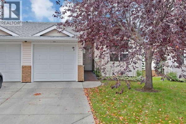 Close-up of townhouse exterior with a single garage door and entryway. - 104 Catalina Circle Ne, Calgary