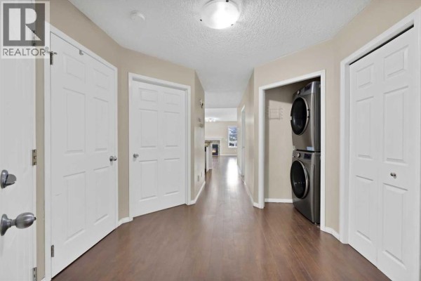 Interior hallway with dark wood floors, white doors, and stacked washer and dryer. - 104 Catalina Circle Ne, Calgary