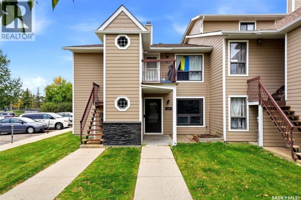 Front exterior of a beige townhouse with external staircases on both sides and a small balcony. - 104 Cedar Meadow Drive, Regina