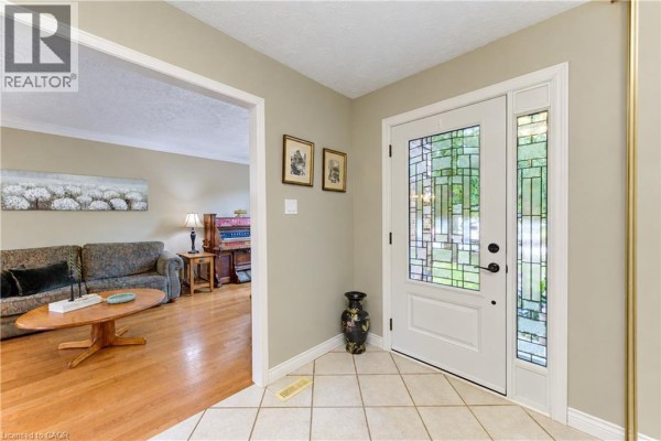 Entranceway with tiled floor, white door, stained glass sidelights, and view into living room. - 104 Deerwood Crescent, Kitchener