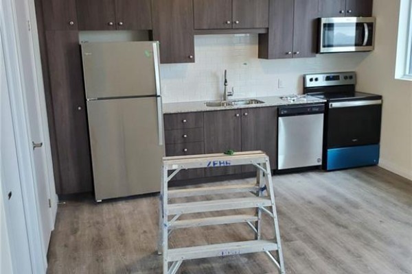 Apartment kitchen with stainless steel refrigerator, dishwasher, microwave, and dark wood cabinets. - 104 Garment Street Unit# 803, Kitchener