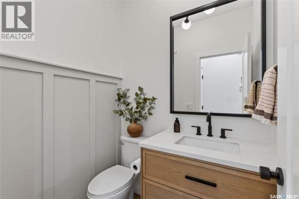 Powder room with a white toilet, wood vanity, white countertop, and black fixtures. - 104 Lakewood Drive, Humboldt