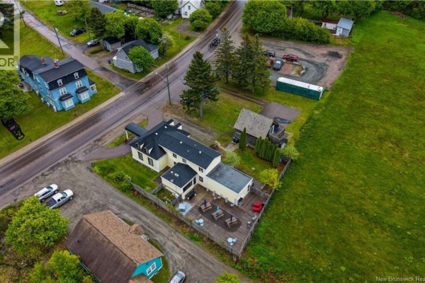 Aerial view of the yellow house and surrounding properties, showing a large wooden deck and driveway. - 104 Main Street, Rexton