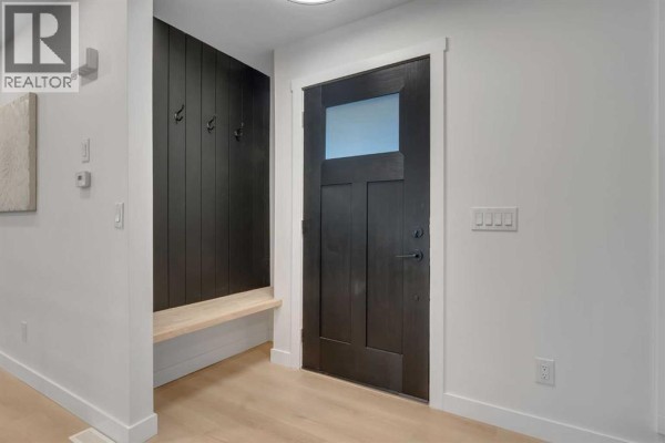 Interior entryway with a dark wood door, a black paneled accent wall with coat hooks, and a light wood bench. - 104 Oakmoor Place Sw, Calgary