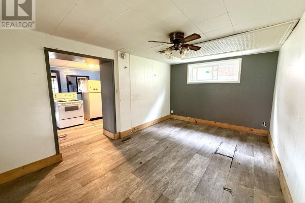 Living area with light wood-look flooring, white paneled walls, dark grey accent wall, and doorway to kitchen. - 104 Ontario Street, Burk S Falls