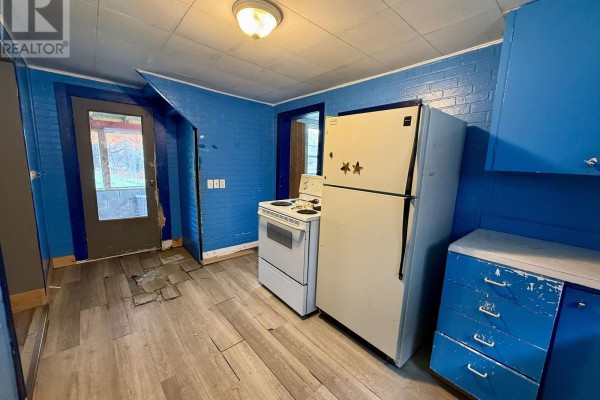 Kitchen with blue painted brick walls, white stove and refrigerator, and a door to an enclosed porch. - 104 Ontario Street, Burk S Falls