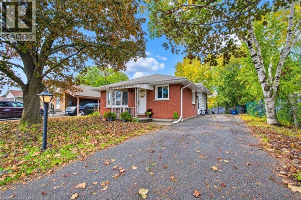 View of red brick bungalow with asphalt driveway and autumn leaves. - 104 Weichel Street, Kitchener