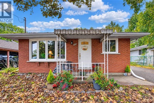 Front entrance of red brick bungalow with white door, windows, and porch. - 104 Weichel Street, Kitchener