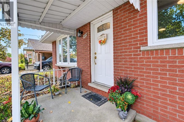 Close-up of bungalow front door with two chairs, potted plants, and brick exterior. - 104 Weichel Street, Kitchener