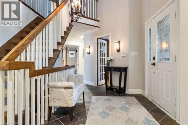 Interior foyer with a dark wood staircase, white banister, tiled floor, and glass-paneled door. - 104 Whittington Place, Oakville