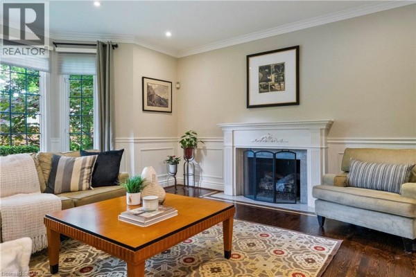 Living room featuring a fireplace, cream-colored sofa, armchair, coffee table, and wood floors. - 104 Whittington Place, Oakville