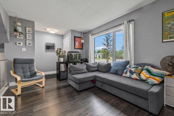 Living room with a grey sectional sofa, a large window with white curtains, and dark wood floors. - 1040 Lakewood Rd N Nw Nw, Edmonton