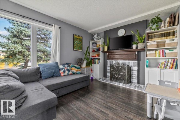 Living room featuring a grey sectional sofa, fireplace with a wooden mantel, and a window with trees outside. - 1040 Lakewood Rd N Nw Nw, Edmonton