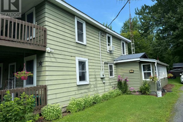 Side view of the two-story green house showing windows, air conditioners, and a small attached room. - 10407 Hainsville Road, South Dundas