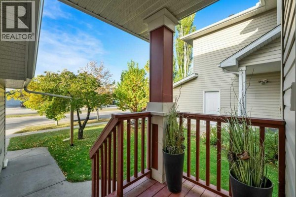 View from the covered front porch with dark red railings and pillars, overlooking a street and trees. - 1041 Cranston Drive Se, Calgary