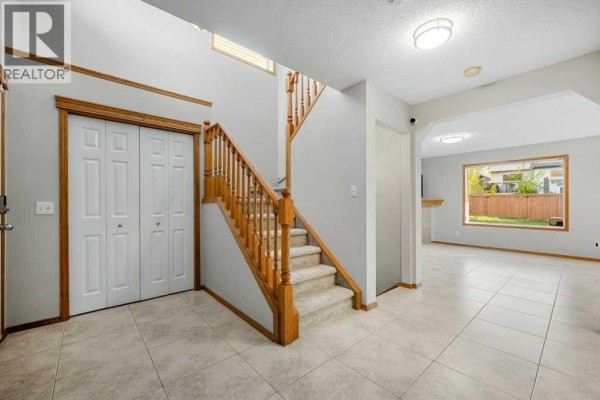 Foyer with beige tiles, carpeted stairs with wooden banister, and an opening to a living area. - 1041 Cranston Drive Se, Calgary