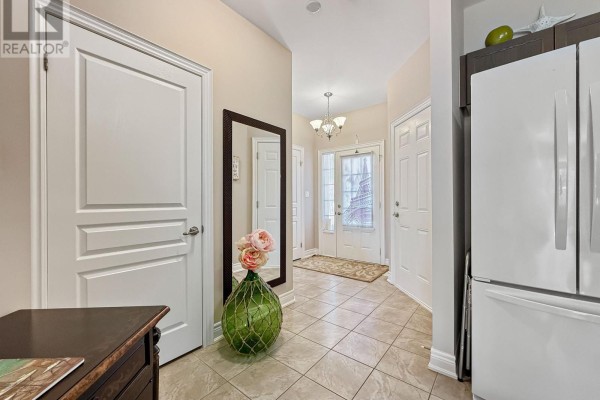 Foyer with tiled floor, beige walls, two white doors, a mirror, and a refrigerator. - 1041 Meadowood Street, Fort Erie