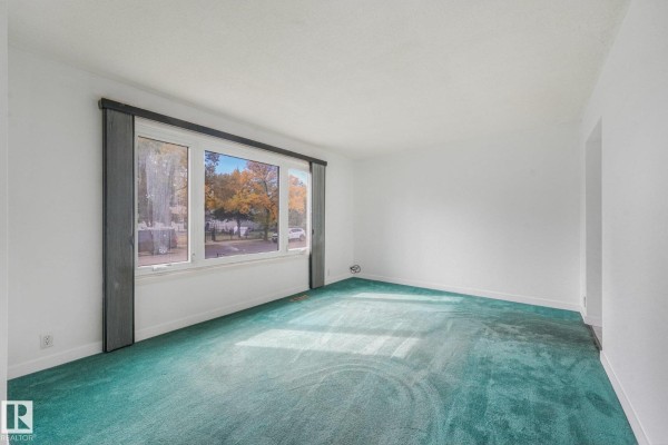 Living room with teal carpet and white walls, showing the large window view. - 10410 Lauder Av Nw, Edmonton