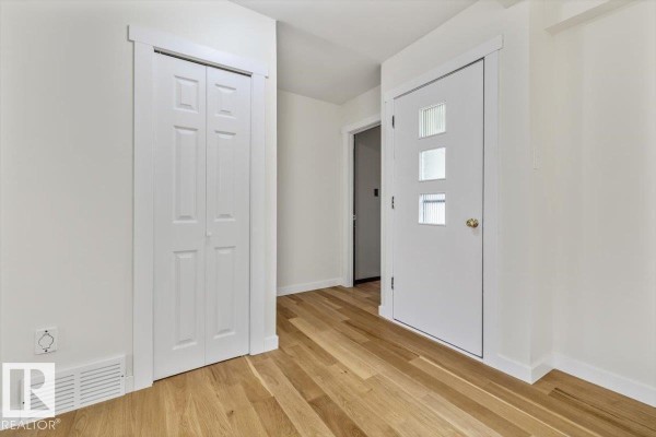 A bright entryway with white walls, light wood floors, a white bi-fold closet door, and a glass-paneled front door. - 10415 98 Av, Fort Saskatchewan