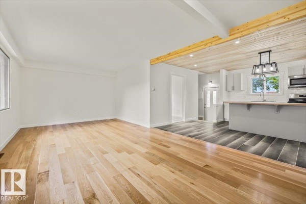 An open living room with light wood floors leading into a kitchen with grey cabinets and a wood-paneled ceiling. - 10415 98 Av, Fort Saskatchewan