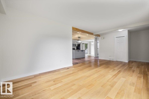 The living room with light wood floors and white walls, looking towards the kitchen and the entryway with glass panels. - 10415 98 Av, Fort Saskatchewan