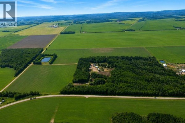 Wide aerial perspective of farmland with agricultural fields, a wooded area, and a farmstead in the distance. - 104262 Rge Rd 151, Rural Mackenzie County