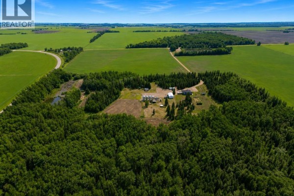 Aerial view of a farm with grain silos and outbuildings situated in a clearing within a vast forest. - 104262 Rge Rd 151, Rural Mackenzie County