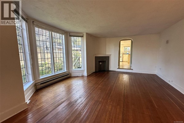 Living room featuring polished hardwood floors, a fireplace, and an arched doorway. - 1043/1045 Belmont Ave, Victoria