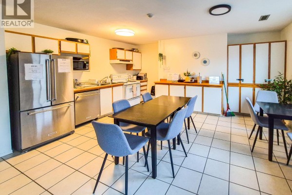 Interior common area with stainless steel appliances, a large dining table, grey chairs, and white tiled floors. - 1045 Highway 97, Okanagan Falls