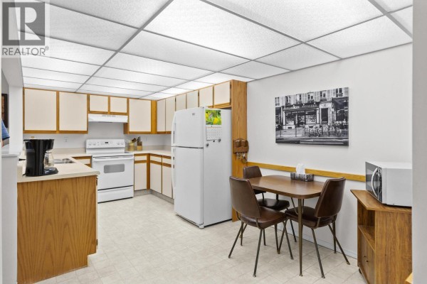 Kitchen area with white appliances, wooden cabinets, and a small dining table. - 1045 Sutherland Avenue Unit# 214, Kelowna
