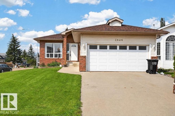 View of the house entrance, garage, and lawn with trees in the background. - 1046 Jones Cr Nw, Edmonton