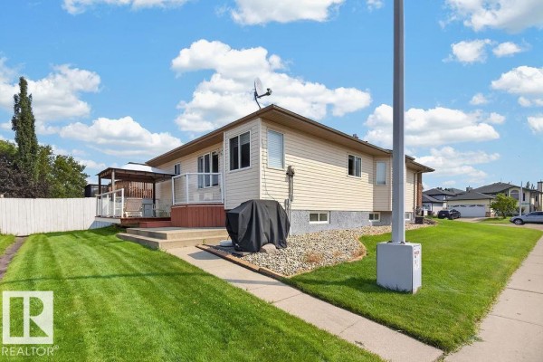 Backyard view of the house with a wooden deck, covered patio, and grassy lawn. - 1046 Jones Cr Nw, Edmonton