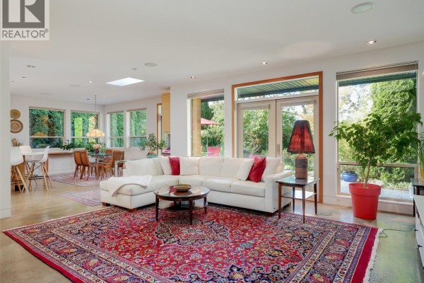 Spacious living room with a white sectional sofa, coffee table, and large windows. - 1047 San Marino Cres, Saanich