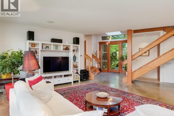 Living room with white entertainment unit, stairs, and view of backyard entry. - 1047 San Marino Cres, Saanich