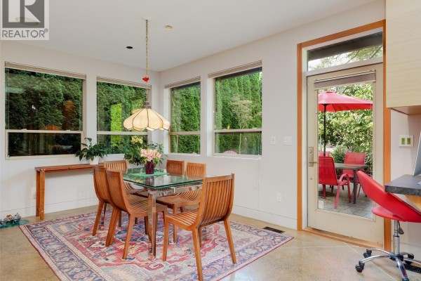 Dining area with a glass table, wooden chairs, and windows overlooking a patio. - 1047 San Marino Cres, Saanich