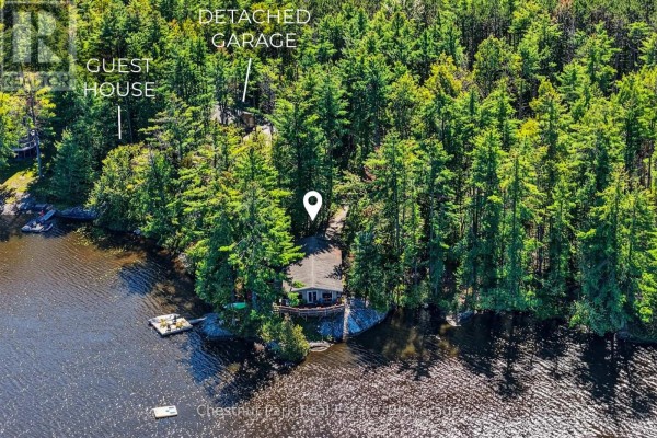 Aerial view of a cottage on a lake surrounded by trees, with labels for guest house and garage. - 1048 Nora Lane, Gravenhurst