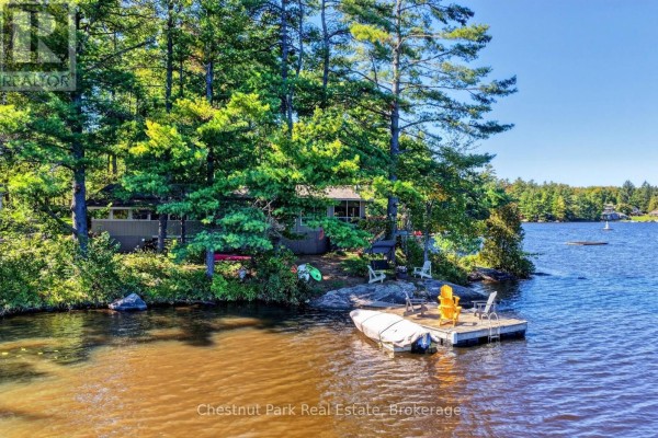 Cottage exterior with a boat on the dock and trees on the property. - 1048 Nora Lane, Gravenhurst