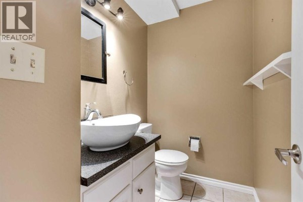 Powder room with a white vanity, vessel sink, black countertop, and toilet. - 105, 107 Elm Place, Okotoks