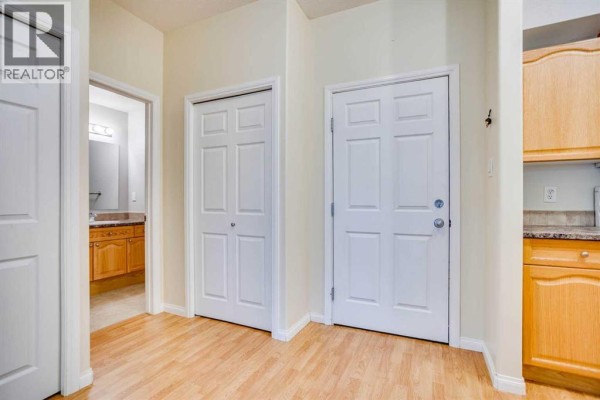 Apartment hallway with beige walls, wood-look flooring, and two white doors. - 105, 290 Plamondon Drive, Fort Mcmurray