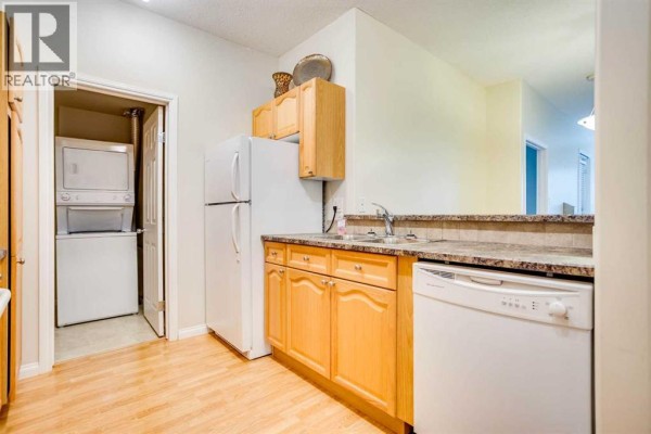 Kitchen with light wood cabinets, white refrigerator, sink, dishwasher, and laundry closet. - 105, 290 Plamondon Drive, Fort Mcmurray
