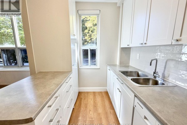 Kitchen with white cabinets, countertop, double sink, and windows overlooking trees. - 105 - 10 Beechwood Place, London South