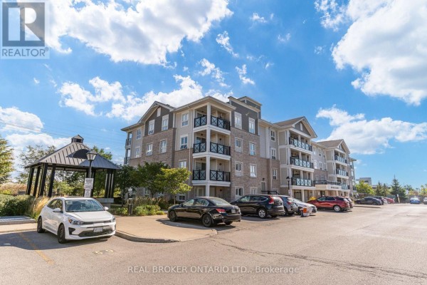 Side exterior view of an apartment building with a parking lot and gazebo in the foreground. - 105 - 1045 Nadalin Heights, Milton