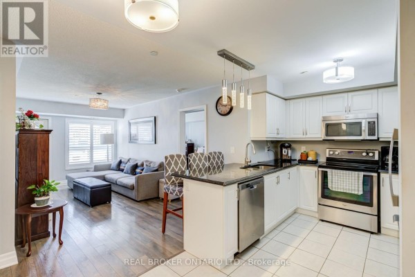 Open concept living and kitchen area with a sectional sofa, island with stools, and white cabinetry. - 105 - 1045 Nadalin Heights, Milton